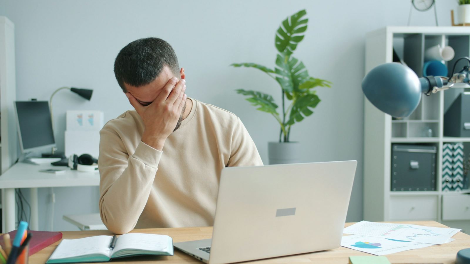 A frustrated man rubbing his face in front of his laptop